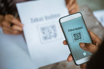 close up of hand paying zakat online using mobile phone and scanning payment barcode