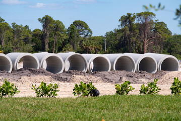 Large concrete water pipes lying on a construction site on a field to build a drainage sewage system against flooding
