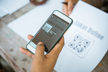 close up of hand paying zakat online using mobile phone and scanning payment barcode