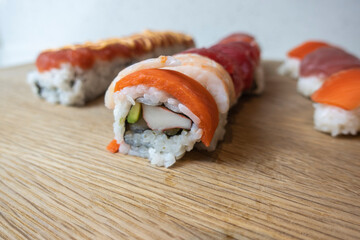 Angled, selective focus view of a variety of sushi rolls on a bamboo cutting board