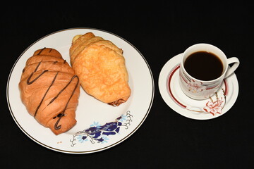 porcelain platter with Croissants, and a cup of coffee on black background