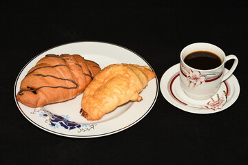 porcelain platter with Croissants, and a cup of coffee on black background
