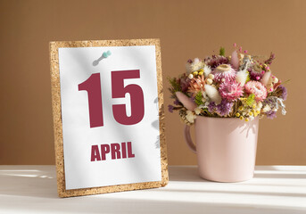April 15. 15th day of month, calendar date.Bouquet of dead wood in pink mug on desktop.Cork board with calendar sheet on white-beige background. Concept of day of year, time planner, spring month