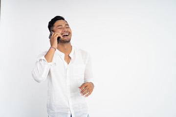 young asian man wearing white shirt laughing while making phone call on isolated background
