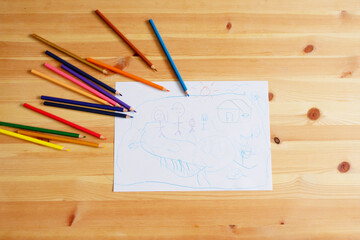 Cute Asian boy drawing happy family and home. with color pencils and white paper on wooden table, top view