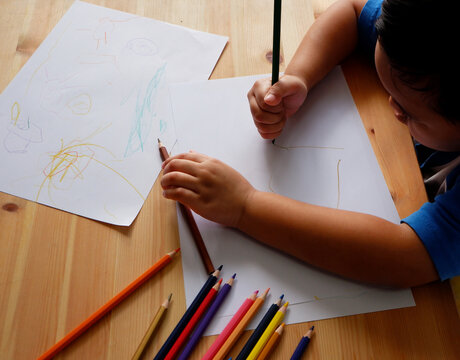Cute Asian boy drawing with color pencils and white paper on wooden table