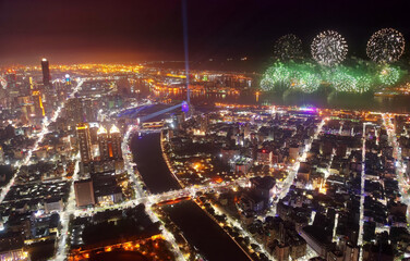 Fototapeta na wymiar Aerial panorama of Kaohsiung City at dusk, a vibrant seaport in South Taiwan, with the landmark 85 Sky Tower standing among skyscrapers by the harbor & street lights dazzling with fireworks at dusk