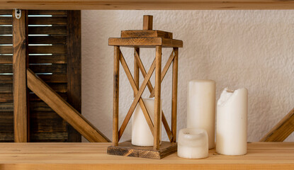Old wooden decorative lamp and paraffin candles stand on shelf. Decor of modern apartment in retro style.