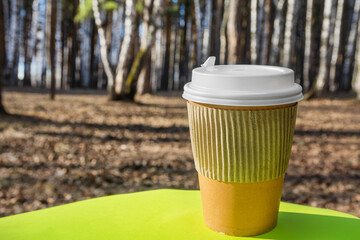 Paper cup for coffee with a plastic lid on a nature background. Environmental pollution with household waste