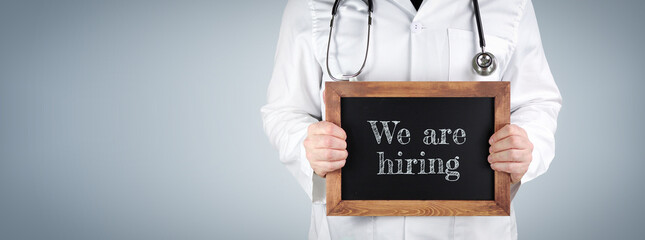 We are hiring. Doctor shows term on a wooden sign.