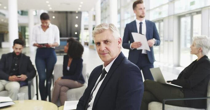 I'm always making a move. Handsome happy mature confident corporate business man looking at camera while sitting in front of a group of diverse and different aged business people in a modern office