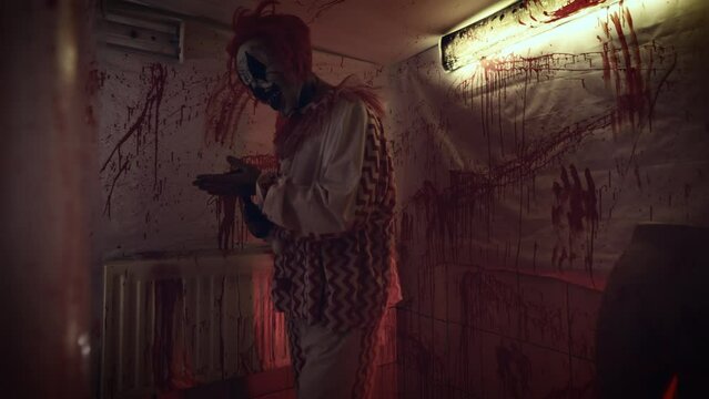 Crazy maniac in a clown costume in his bloody lair. Terrible image from nightmares.