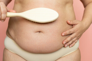 Cropped overweight woman belly with navel in pants with excessive weight, visceral fat abdomen. Dry brush massage by natural stubble, rubbing skin. Make skin turgor, get rid of hanging tummy. Home spa