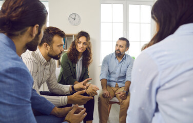 Different people sitting in circle and listening to therapist during group therapy session meeting. Group of people talking, discussing mental problems and issues, trying to cope with them together