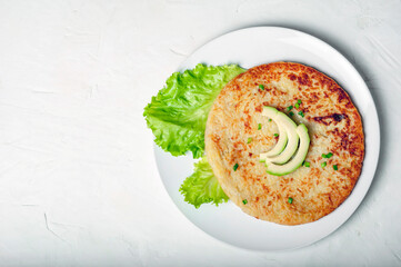 traditional Swiss dish is a potato pancake on a white plate, decorated with a leaf of green salad and avocado, copy space, top view.