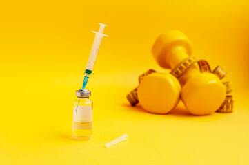 syringe is stuck in a jar, dumbbells and a measuring tape on a yellow background are lying next to...