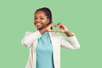 Happy beautiful black woman makes heart with hands. Young Afro American girl standing on green...