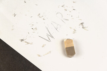 Half-erased with an eraser is the word WAR. Handwritten word on white paper.