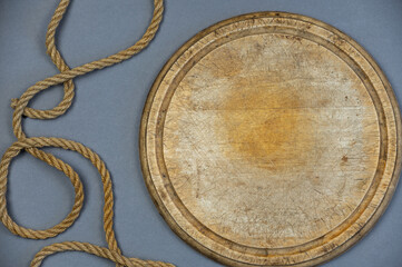 Round wooden cutting board and ship's rope against the gray background. An old empty cutting board. Jute rope. Top view.