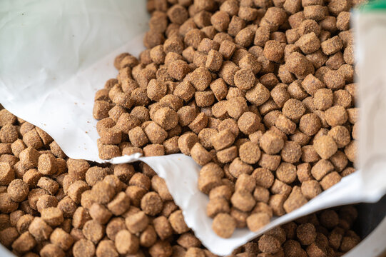 Close-up of dry pelleted pet food. Brown round pellets inside an open white bag. Pet food.