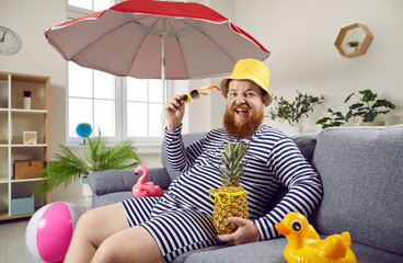 Funny bearded guy spends summer holiday on pretend beach at home. Plus size man in swimsuit and hat...