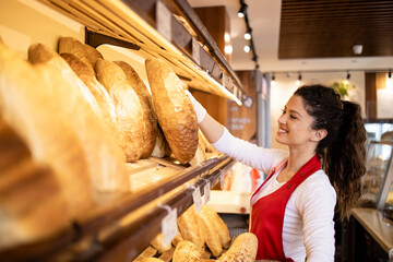 Working in bakery shop arranging freshly baked loafs of bread on the shelf.