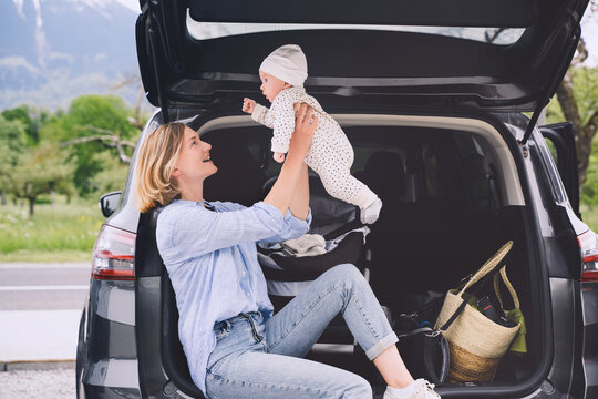 Mother with baby sitting in open car trunk outdoors. Road trip with baby. Travel in Europe. Young mother with her little baby having picnic near by the car. Safety driving by car with small kids.
