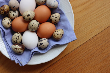 Fresh chicken brown and white eggs and quail eggs in a bowl on wooden table