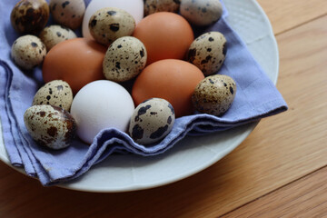 Fresh chicken brown and white eggs and quail eggs in a bowl on wooden table