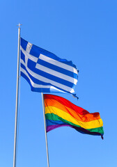 Flag of Greece and LGBT flags are fluttering in the wind against the blue sky