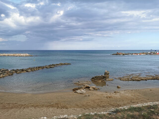 Fototapeta na wymiar Bay of the Mediterranean Sea, sandy shore with a stone ridge and stones against a dramatic sky.
