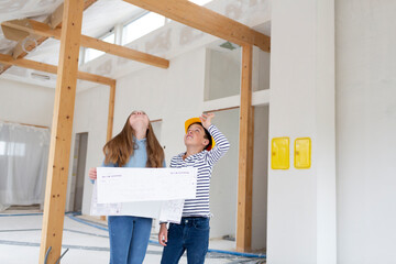 Brother and sister are on the construction site of their new room loft apartment with plan and yellow helmet and check the progress and enjoy