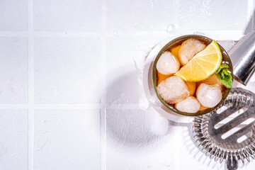 Rum, Lime and Cola Cuba Libre Cocktail. Summer cold Coca Coke drink with citrus juice, ice cubes and mint leaves, white tiled sun lighted background copy space
