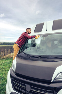 Young man cleaning camper van windshield with sponge outdoor