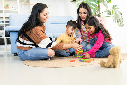 A young lesbian family with two children, Hispanic, a son and a daughter, spends time at home. They sit by the sofa and play. Marriage of a homosexual couple.