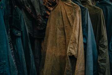 Fototapeta premium Hanger stand with vintage wax jackets. Secondhand brown jackets ,sweater and different Winter jackets. Men's wax jackets on hangers outdoors.