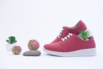 A pair of burgundy shoes in a shop window. The concept of environmentally friendly shoes. Shoes made from recycled materials. Nature design elements: grass, flowers and stones