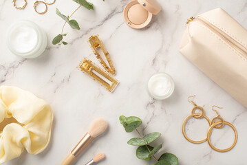 Top view photo of golden barrettes cream bottles eyeshadow scrunchy makeup brushes golden earrings rings cosmetic bag and eucalyptus on white marble background