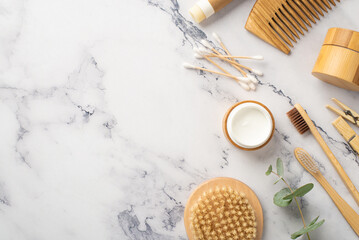 Top view photo of anti-cellulite washcloth wooden bottles bamboo hairbrush cream jar toothbrushes cotton buds clothespins and eucalyptus on white marble background with copyspace