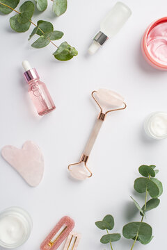 Top view vertical photo of rose quartz roller gua sha pink eye patches bottles with cosmetics barrettes and eucalyptus on isolated white background
