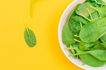 Fresh Baby Spinach Leaves in White Bowl on Yellow Background - Top View. Vegan and Vegetarian Culture. Raw Food, Green Leaves. Healthy Diet