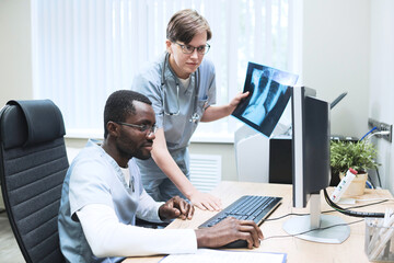 Young multi-ethnic medical specialists using computer while doing MRI and analyzing lung lesions of covid patient
