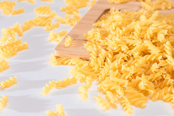 Uncooked Fusilli Pasta Scattered on Wooden Board and White Table. Raw and Dry Macaroni. Fat and Unhealthy Food
