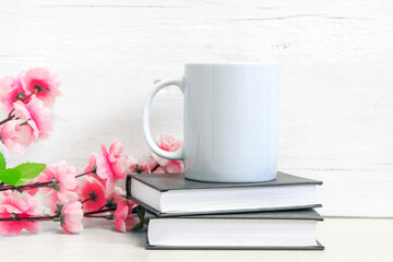 Mockup of a white ceramic mug on a table with books and flowers
