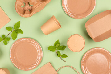 Flat lay composition with eco-friendly tableware and kraft paper food packaging on light green background. Sustainable packaging, recyclable paperware, sustainable food packaging concept