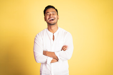 asian young man wearing white shirt laughing with arms crossed on isolated background