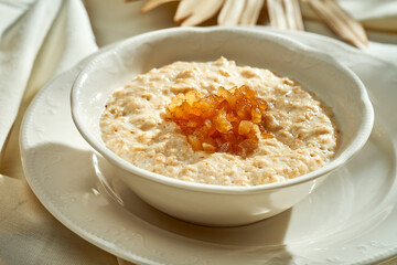 Oatmeal with caramelized apples in a white plate. Hard light. Selective focus.