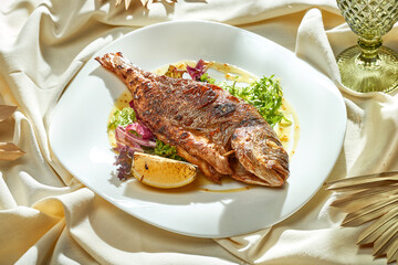 Baked dorado with salad and dressing in a white plate. Hard light. Selective focus.