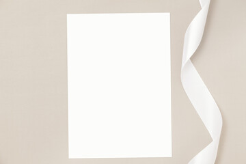 Wedding invitation or greeting card mockup with white satin ribbon on a beige background. - obrazy, fototapety, plakaty