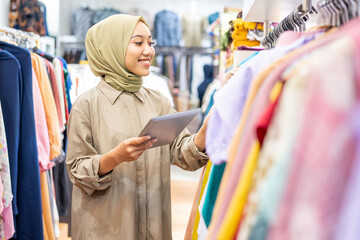 veiled woman hold tablet while working in Muslim clothing store